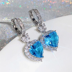 Close-up of heart-cut blue topaz earrings with silver pavé setting and sparkling crystals