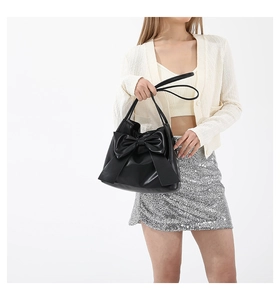 Detail of black matte leather tote featuring a large decorative bow and long handles