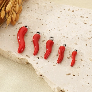Five assorted sizes of 3D red enamel chili pendants arranged on a natural stone tile