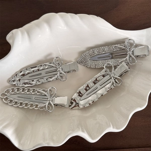 Detail of four silver metal bow hair clips with rhinestones and chain patterns in a shell tray