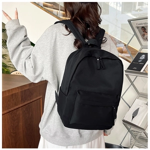 Rear view of model wearing a large black nylon backpack with front pocket details