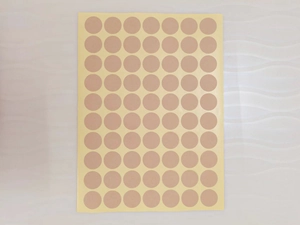 Macro view of round beige adhesive screw hole covers arranged on yellow backing paper
