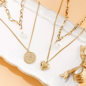 Collier multicouche doré avec perle baroque, pendentif cœur et pièce sur un plateau