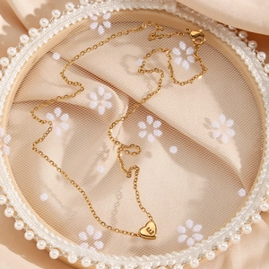Détail du pendentif coeur doré avec gravure lettre E sur fond de dentelle élégante