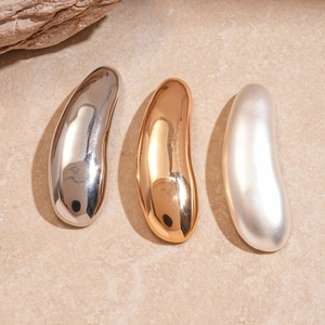 Detailed view of drop-shaped metal brooches in polished gold, silver, and matte finish