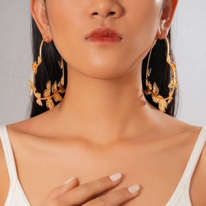 Dettaglio di grandi orecchini a cerchio dorati a forma di cuore con farfalla indossati dalla modella