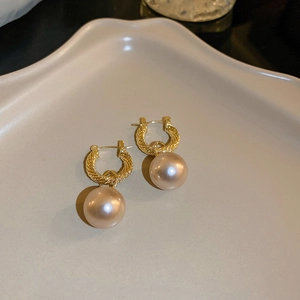 Detail of gold twisted hoop earrings with champagne pearls on a cream wavy tray