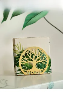 Detail of golden life tree metal napkin holder on marble surface with green leaf background
