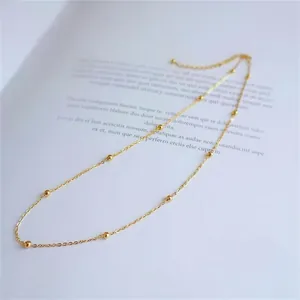 Minimalist gold titanium necklace featuring small beads on a white book backdrop
