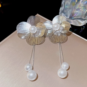 Macro shot of long silver floral earrings with glossy white pearls and tassel chains