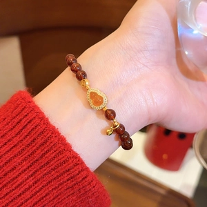 Detailaufnahme eines roten Achat-Perlenarmbandes mit goldenem Kürbis-Anhänger.