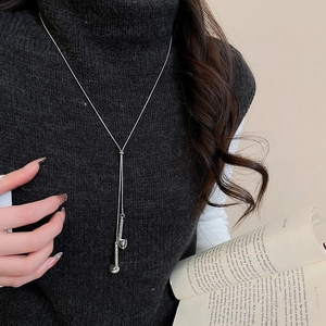Silver long necklace with twin pendants worn over a black turtleneck sweater