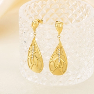 Golden teardrop earrings with crystals hanging on a glass rim in warm lighting