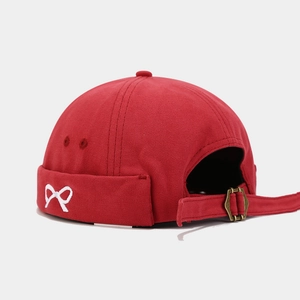 Detailed view of red canvas docker hat with white bow embroidery and bronze buckle