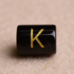 Macro shot of a black rectangular bead with a gold-stamped letter K for DIY jewelry
