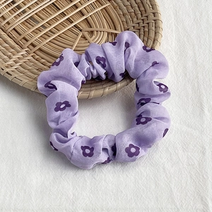 Detailed view of a purple floral scrunchie with satin texture in a woven tray