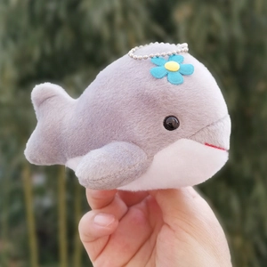 Close-up of a cute grey whale plush keychain featuring a small blue flower detail on top