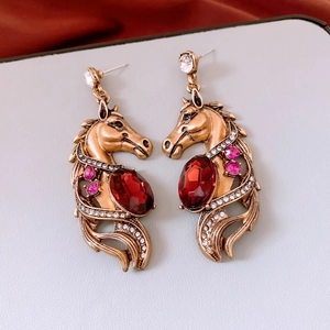 Close-up of vintage gold horse earrings with red crystal pendant and rhinestone details
