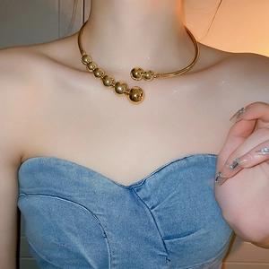 Close-up of a gold chunky metal bead choker necklace worn on the neck with open design