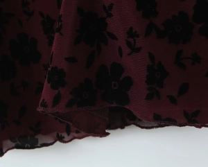 Macro detail of wine red mesh fabric with black floral flocking and lettuce edge hem