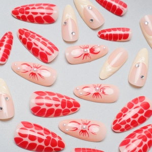 Long almond press-on nails featuring red scale patterns, white pearls, and rhinestones