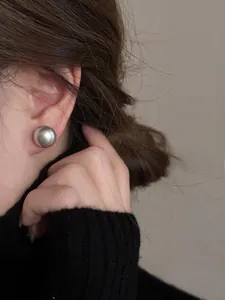 Primo piano di una modella con grandi orecchini a lobo sferici in argento opaco stile retrò