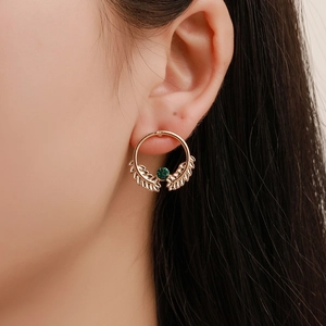Detail of leaf-patterned golden earring with a round green gemstone on a female model