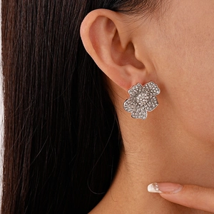 Close-up of minimalist silver flower stud earrings with sparkling crystals on ear