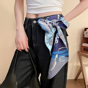 Dettaglio di un foulard in seta blu con stampa equestre annodato come cintura su jeans