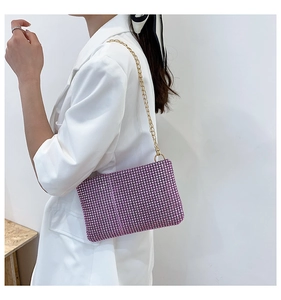 Detail of purple rhinestone handbag with golden chain strap against a white blazer