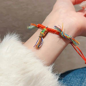 Détail d'un bracelet tissé rouge avec perle en émail doré et pompon multicolore
