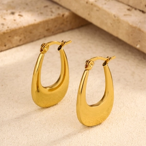 Close-up of golden U-shaped stainless steel earrings on a beige stone background