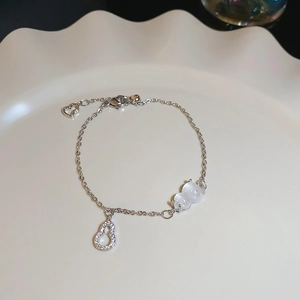 Macro shot of silver zircon flower bracelet with white opal gourd pendants in a ceramic plate