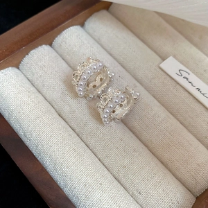 Macro shot of silver crown lace pearl earrings on a beige velvet jewelry display