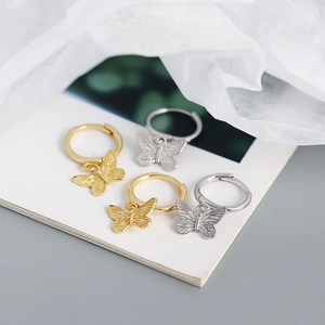 Detalle de pendientes de mariposa en color oro y plata sobre fondo de tela blanca suave