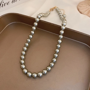 Elegant grey pearl necklace with golden clasp displayed on a luxury gold tray