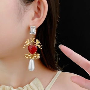 Detail of vintage gold earrings with red heart, angel motifs, and white pearl droplet