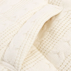 Detail of a creamy white knit vest showing side pocket and soft cable texture