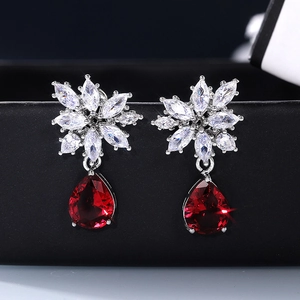 Detail of flower shaped earrings with white zircons and a large red pear-cut drop