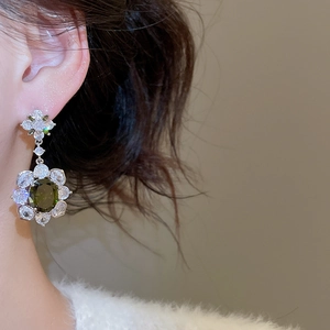 Close-up of vintage flower earrings with olive green gems and sparkling zircons