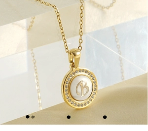 Vue macro du pendentif en acier doré avec lettre B, incrustation nacre et oxydes de zirconium