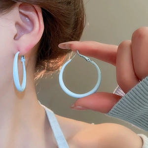 Detail view of stylish light blue hoop earrings with smooth lacquer finish on model