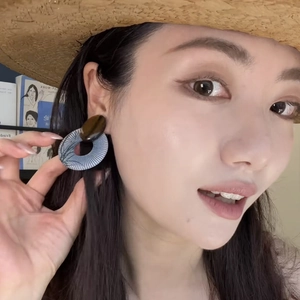 Blue round resin dangle earrings with radial texture worn by a model in a summer setting