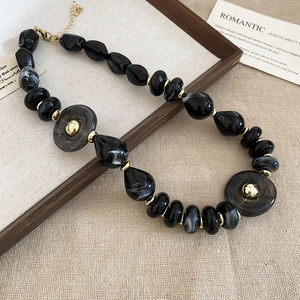 Close-up of black and marble acrylic beaded necklace with golden metal accents on fabric