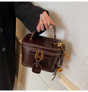 Detail of dark brown box bag with shiny leather texture and golden metal accents