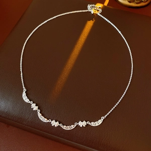 Close-up of a silver bow necklace with hollow wave patterns on a brown leather surface