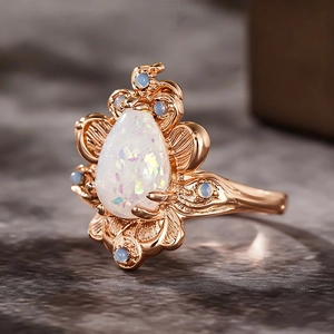 Macro detail van een bladvormige roségouden ring met druppelopaal en blauwe stenen