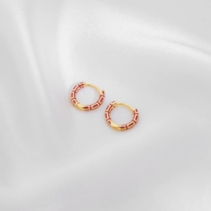 Macro view of gold hoop earrings with red enamel detail on a white silk background