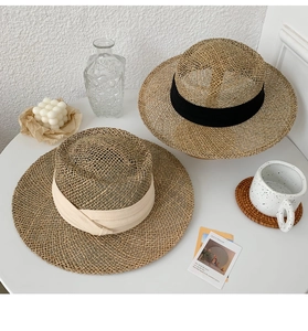 Detail of flat top straw hats with black and beige ribbon bows on a minimalist table