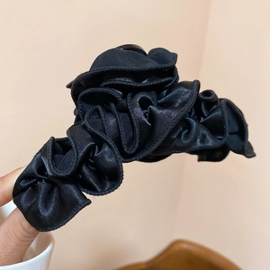 Detail of a black pleated satin fabric hair clip with elegant ruffled texture